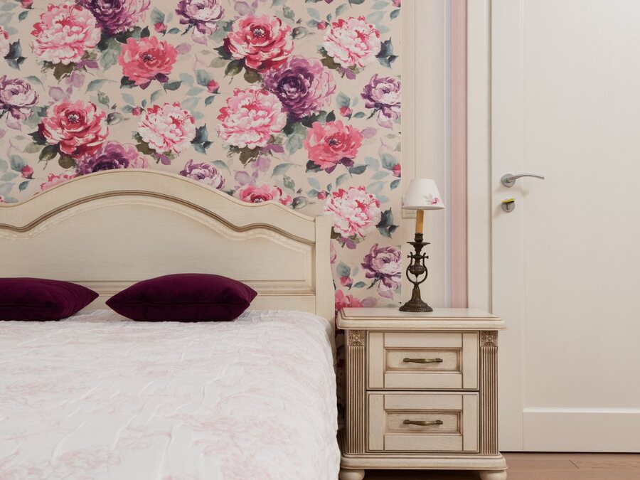 Bedroom with large-scale pink floral botanical wallpaper behind a cream headboard.