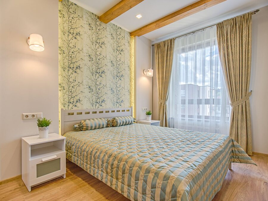 Bedroom with warm decorative toile wallpaper and soft gold-toned curtains by the window.