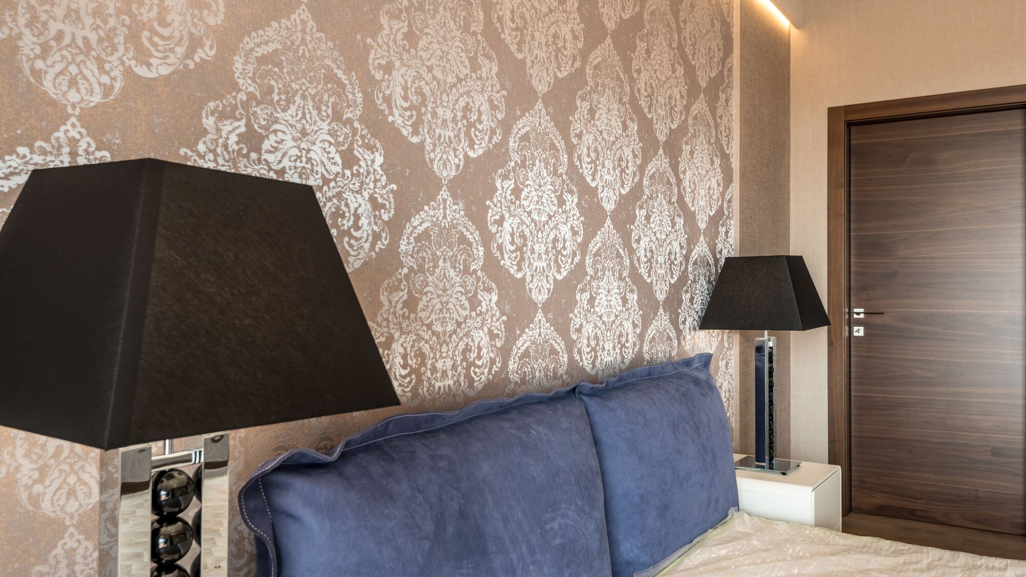 Elegant bedroom with warm damask patterned wallpaper behind the bed, softly lit by bedside lamps.