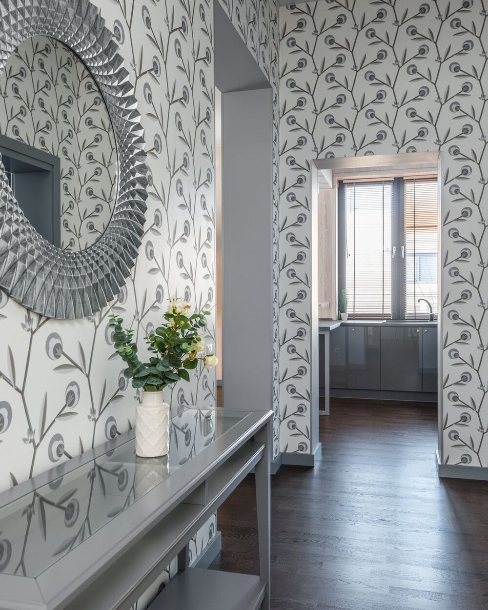 Hallway with a delicate leaf-motif wallpaper, an ornate round mirror, and a slim console table with fresh flowers.